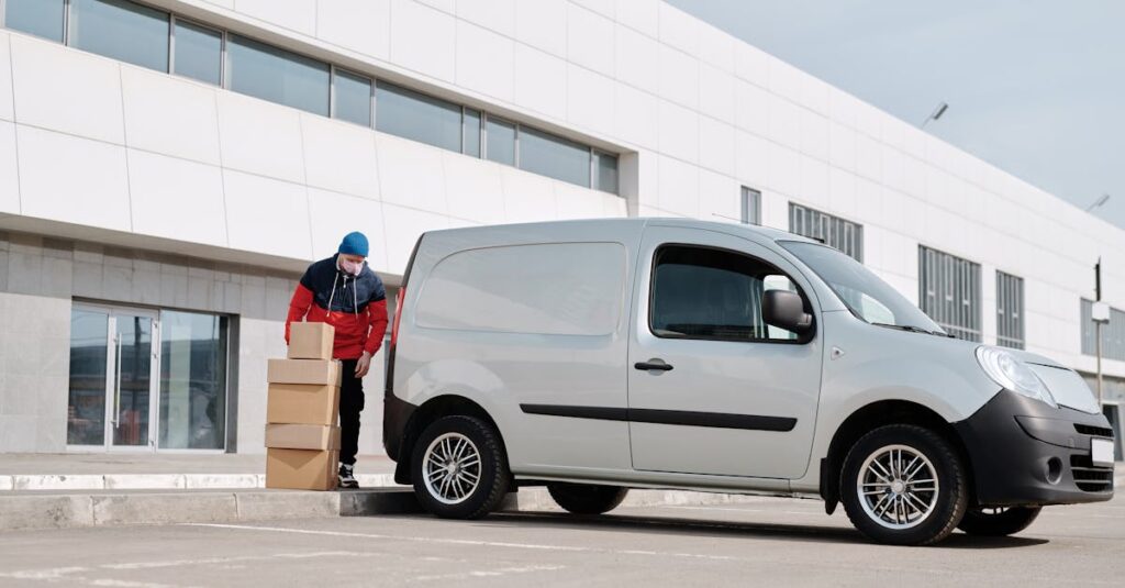pexels-photo-4391470-4391470 A delivery driver wearing a face mask unloads packages from a van outside a modern building.